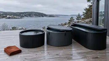 Tre isbade på en våd træterrasse ved vandet: et lille rundt, et rundt med låg og et langt ovalt, med et rødbrunt håndklæde foran